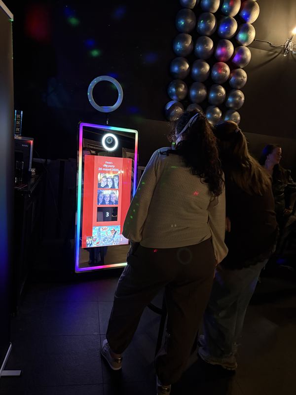 Gasten bekijken samen hun fotostrip bij de Magic Mirror tijdens een verjaardagsfeest met discoballen